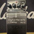 Šedý kytarový efekt s nápisem Digital Reverb / Delay RV-3 a logem BOSS na spínacím pedálu. Na horní části jsou čtyři černé otočné ovratky a přepínače…
