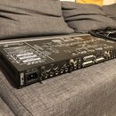 Černý rackový audio konvertér s kovovým šasi a integrovaným schématem na horním krytu. Na zadním panelu jsou vidět různé konektory, včetně vstupů pro…