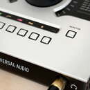 Detailní záběr na stříbrnopřední panel audio rozhraní s černým bočním profilem. Na černé části je bílý nápis UNIVERSAL AUDIO s doprovodným logem. Na…