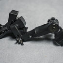 Černý kovový držák s ramenem a dvěma svěrkacími mechanismy. Na pravém konci je viditelný nápis X-PRO. Povrch vykazuje mírné známky opotřebení a prach.