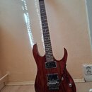 Elektrická kytara s červeně stříbřitým dřevěným povrchem a hnědým hmatníkem. Na hlavě je bílý nápis Ibanez. Nástroj má dva humbuckery, Tremolo systém…