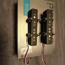 Dvě černé humbuckery s kovovými zlatými šrouby a připojenými červenobílými vodiči. Na obou snímačích je v dolní části zlatý nápis EMG X. Snímače leží…