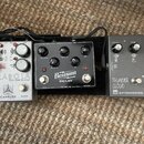 Tři efektové pedály umístěné vedle sebe na hnědém koberci. První pedál je bílý s nápisy PARABOLA, SOLID STATE TREMOLO a CAROLINE CUSTOMER COMPANY. Pr…