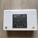 Fotografie znázorňuje bílý karton s produktem Behringer MIC300. Na krabici je nápis MIC300, Audiophile Vacuum Tube Preamplifier with Limiter a logo b…