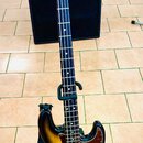 Elektrická basová kytara s korpusem v přechodovém žlutomodrém odstínu (sunburst) a tmavým hmatníkem. Na hlavě je viditelné logo "Fender". Kytara má č…
