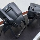 Dvě černé světelné reflektory na stojkách umístěné na černém povrchu v přepravním kufru. Zařízení mají plastové provedení s ventilačními mřížkami a j…