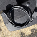 Černý napájecí kabel srolovaný do kruhu, položený na texturovaném černém povrchu. Kabel má na koncích standardní plastové konektory. Na povrchu kabel…