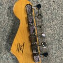 Zadní strana hlavy kytary z přírodního dřeva s chromovanými ladicími kolíky. Na dřevě je černý nápis: Designed and Backed by Fender s/n ISSK20003917…