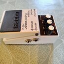 Bílý kytarový pedál s černým nášlapným spínáčem, na kterém je vyražen nápis BOSS. Na horní straně jsou texty Noise Suppressor NS-2 a označení vstupů…