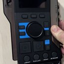 Černý elektronický přístroj s displejem a ovládacími prvky. Na levé straně je bílé logo s písmenem B a nápisem BEAT. Na spodní části jsou tlačítka s…