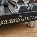 Detailní záběr na černý kovový most hudebního nástroje. Na boku je bílý nápis „aclam GUITARS“ s malým trojúhelníkem nad písmenem M a symbolem ® v pra…