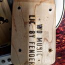 Záběr na zadní stranu dřevěné hlavy kytary. Na dřevě je vyryt nápis WD MUSIC LIC. BY FENDER. V horní a spodní části jsou vidět čtyři otvory pro ladič…