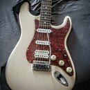 Bílá elektrická kytara s hnědým vzorovaným pickguardem. Na spodním snímači je viditelný nápis Seymour Duncan. Kytara vykazuje známky opotřebení v pod…
