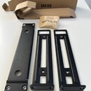 Tři černé kovové montážní lišty různých tvarů a jeden papírový sáček s nápisem Mounting Kit. V pozadí je hnědá kartonová krabice s vytištěným číslem…