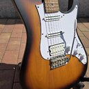 Elektrická kytara s tělem v provedení sunburst a bílým pickguardem. Nástroj má dva snímače typu humbucker a jeden snímač typu single-coil, chromovaný…