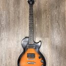 Elektrická kytara s tónem sunburst v oranžovo-černé kombinaci a tmavým hmatníkem. Na hlavě je bílý nápis Epiphone a pod ním stylizovaný nápis Les Pau…