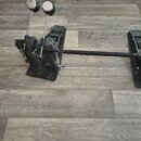 Černý dvojpedál na bicí buben s kovovým provedením. Pedály mají vroubkované stupnice a dvě nastavitelné páky s černobílými knoflíky. Na komponentech…
