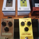Dvě efektové pedály umístěné na černém pedalboardu, vedle nich jsou jejich originální krabice. Levý pedál je hnědý s nápisy tc electronic, Echobrain…