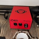 Červené obdélníkové zařízení s logem opice na horní a přední straně. Na předním panelu jsou nápisy Monkey Banana, Mangabey, OUTPUT a INPUT u příslušn…