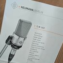 Fotografie zachycuje obálku uživatelské příručky k mikrofonu. Je na ní vidět stříbrný kondenzátorový mikrofon s nápisem NEUMANN BERLIN a logo značky.…