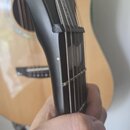 Detailní pohled na hmatník a horní část krku akustické kytary v černé barvě. Na hraně hmatníku je viditelné odřasení laku a drobné poškození povrchu.…