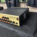 Kovový hybridní zesilovač s černým horním krytem a zlatým předním panelem. Na panelu je nápis The Traveler 550 Wood Four Class Hybrid Bass Guitar Amp…