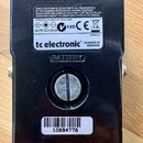 Zadní strana černého efekt pedálu s čtyřmi světlými gumovými nožičkami. Na spodní části jsou vidět nápisy „tc electronic“ a „DESIGNED IN DENMARK“, na…
