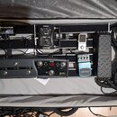 V otevřeném kufru je umístěna pedálboard s několika efekty a napájecím zdrojem. Vlevo nahoře je napájecí jednotka s nápisy PEDALPOWER a LEWITT. Na de…