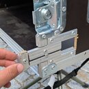 Detailní záběr na poškozený roh černého transportního kufru s hliníkovými profily. Hliníkové lišty jsou v místě spoje přetržené a vyhnuté, je vidět v…