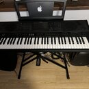 Černý digitální klavír s bílými a černými klávesami umístěný na černém X-stojanu. Na ovládacím panelu je nápis YAMAHA a označení modelu SX700. Na při…