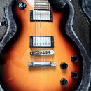Elektrická kytara s tmelem v odstínu sunburst, umístěná v otevřeném pouzdře s šedým polstrováním. Nástroj má dva humbuckery s bílými kryty, chromovan…