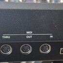 Detail zadní strany černého hudebního nástroje s řadou připojovacích konektorů. Nad konektory jsou bílé nápisy: OUTPUT R, L/MONO, PEDAL SUSTAIN, EXPR…