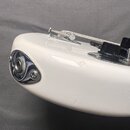 Detailní pohled na bílé tělo elektrické kytary. Je vidět chromovaný výstup pro kabel a část tremolo systému s černými ovládacími knoflíky. Povrch lak…