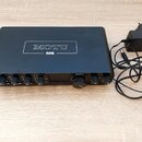 Černý audio rozhraní s nápisem MOTU M6 na horním krytu. Na předním panelu jsou ovládací knofíky, nápis MOTU u displeje a v levém horním rohu žlutá ná…