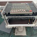 Černý transportní case s hliníkovými hranami, v němž je osazen mixážní pult a rackové zařízení. Na horní části jsou vidět nápisy PHONIC na obou stran…