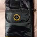 Černý textilní obal na hudební nástroj s žlutým pruhem v dolní části. Uprostřed je kulatý žlutý štít s nápisy ROCKBAG by Warwick, proudly made with R…