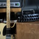 Na fotografii je elektrická kytara typu Telecaster v krémové barvě s černým pickguardem a javorovým hmatníkem. Vedle ní stojí černý kompaktní zesilov…
