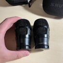 Dvě černé fürheadové kapsle s mřížkou. Na obou je vidět nápis SHURE, na pravé kapsli je dále uveden model NXN8/C. V pozadí je černý obal s nápisem SH…