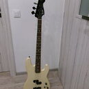 Elektrická basová kytara v krémové barvě s hnědým hmatníkem. Na hlavě nástroje je viditelné logo Fender. Tělo má dva snímače a čtyři ovládací knoflík…