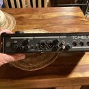 Zadní strana černého elektronického zařízení s nápisem TCHELLI. Jsou zde viditelné vstupy a výstupy označené jako INPUTS (THRU, GUITAR), OUTPUTS (L M…