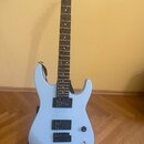 Světle modrá elektrická kytara s černým hmatníkem a dvěma černými humbuckery. Na hlavě krku je viditelna část bílého nápisu "Ja". Nástroj je umístěn…