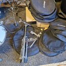 Na fotografii je chromovaný stojan na činely, černý kulatý obal s bílým nápisem "globalbags" a další černý kulatý obal, na kterém je částečně viditel…