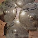 Pět zlatavých činelů s perforovaným povrchem v podobě husté sítě malých otvorů. Každý činel má černý nápis Millenium STEEL CYMBALS. Činely mají různé…