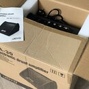 V kartónové krabici s polystyrenovými vložkami je umístěn černý zesilovač. Na zadním panelu přístroje jsou vidět ovládací prvky a konektory, k zaříze…