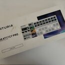 Bílá papírová krabice s nápisy ARTURIA® a BEATSTEP PRO Controller & Sequencer. V dolní části je obdélník s textem PERFORM. Na krabici je zobrazen pro…