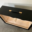 Černý obdélníkový reproduktorový box s povrchem z textilie. Na horní straně je umístěna černá úchytka s dřevěnými zakončeními. Vnitřní prostor boxu j…