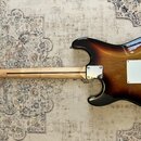 Zadní pohled na elektrickou kytaru s trupem v barevném přechodu od černé k žluté (sunburst). Kytara má světlý dřevěný krk a hmatník. Na zadní straně…