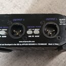 Černý kovový přístroj s dvěma XLR výchyty označenými jako OUTPUT 1 a OUTPUT 2. U každého výstupu jsou přepínače s nápisy GROUND LIFT a PHASE INVERT,…