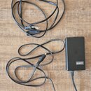 Černý síťový adaptér značky YAMAHA s připojeným kabelem a konektorem. K adaptéru patří samostatný černý napájecí kabel s vidlicí. Vše je položeno na…