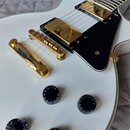 Bílá elektrická kytara s gold hardwarem a černým pickguardem. Nástroj má dva humbuckery, Tune-o-matic kobylku a čtyři černé oválné knofíky s bílým čí…